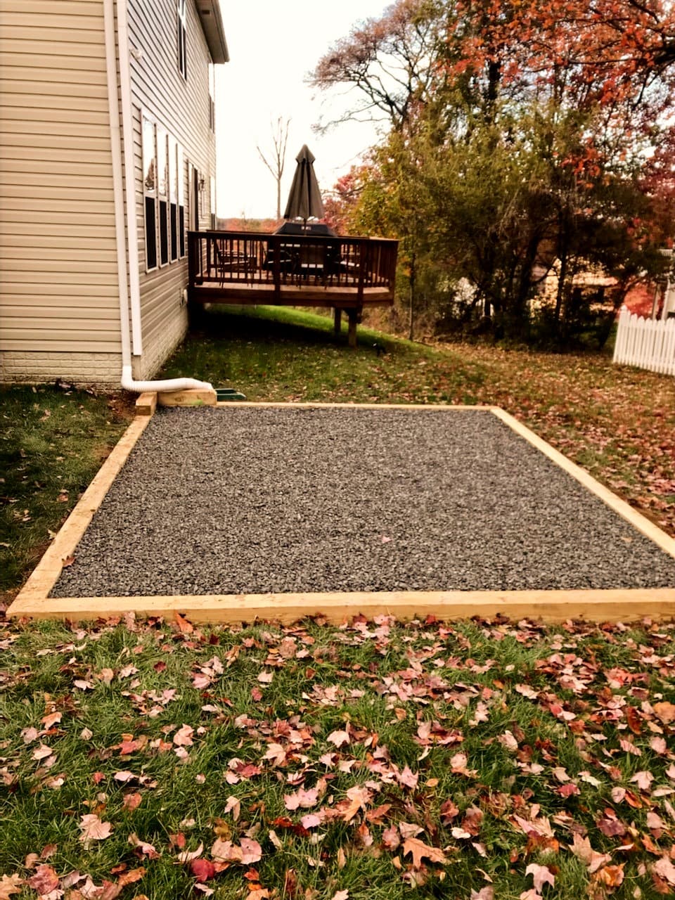 Gravel pad in a fenced backyard surrounded by fall leaves