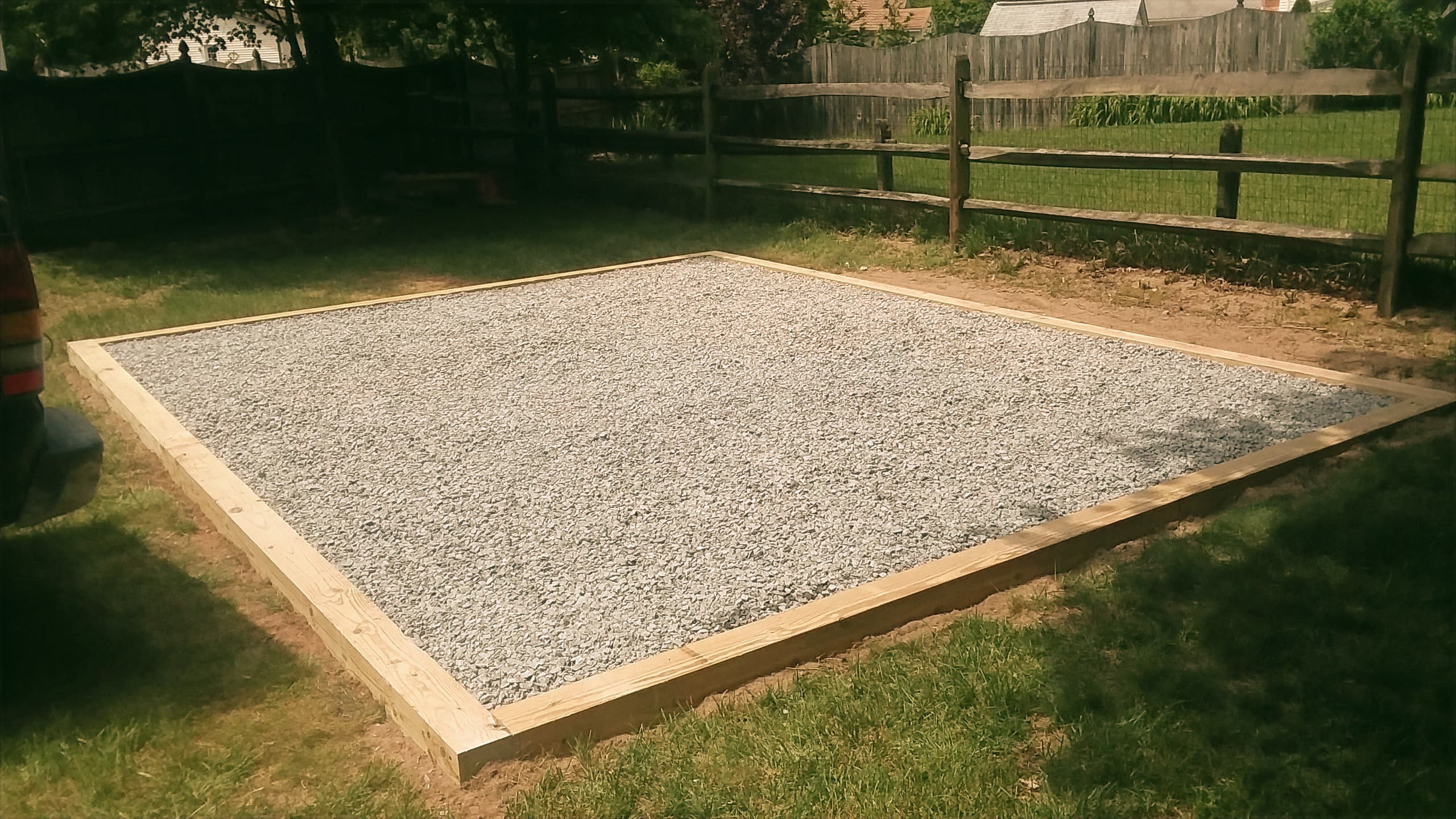 Rectangular gravel pad with a pressure-treated wood frame on a level lawn